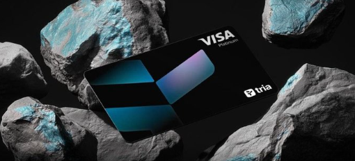 The image features a black Visa credit card placed on top of some rocks. The rock collection includes various sizes and shapes of rocks, creating an interesting visual contrast with the sleek design of the credit card. The text "Visa" is prominently displayed in white letters above the credit card, indicating its purpose as a payment method. The image also contains a caption that reads: "The real flex isn't holding crypto It's being able to do something with it @useTria makes that feel simple: swap across chains, spend with a card, earn along the way This is where Web3 starts feeling normal".