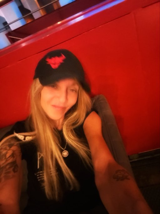 Selfie of a smiling blonde woman wearing a black cap with a red logo, sitting in a red booth.