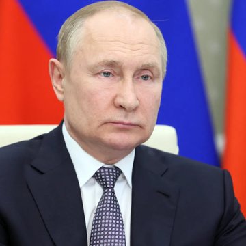 A serious-looking man in a dark suit and patterned tie sits in front of Russian flags, appearing to be Russian President Vladimir Putin. The image relates to the announcement that Russia has begun paying some employees in digital rubles (CBDC), marking a significant step in the country's adoption of central bank digital currency.