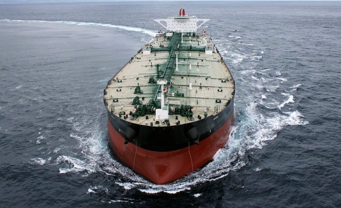 Aerial view of a large red and black oil or cargo tanker ship sailing through dark blue ocean waters.