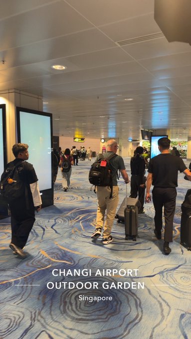 Travelers walk through a corridor at Changi Airport's Outdoor Garden in Singapore, as indicated by the on-screen text overlay referencing the Token2049 crypto conference.