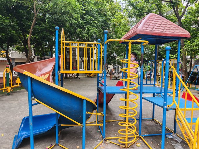 A photo of a blue and yellow plastic playground set with a red slide and spiral climber in an outdoor park setting, with a child partially visible on the structure.