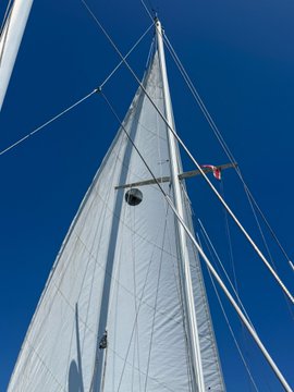 A low-angle shot looking up at the white sail and rigging of a sailboat against a clear blue sky.