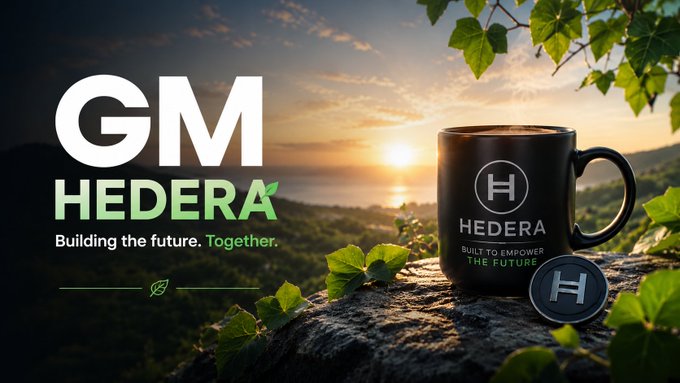 The image features a black coffee mug with a green logo, which reads "GM Hedera", placed on top of a rock. The mug has a silver coin attached to its side. In the background, there are trees and mountains visible, creating an outdoor setting for this scene. The post about GM Hedera is written in white text that says "Building the future Together".