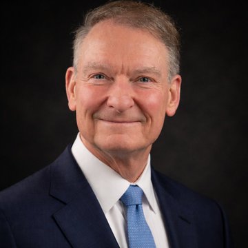 A professional headshot of a smiling older man with short hair, wearing a dark suit and blue tie against a black background—identified in the accompanying text as SEC Chair Paul Atkins, who is reportedly urging the Senate to pass the CLARITY Act to address crypto regulatory uncertainty.