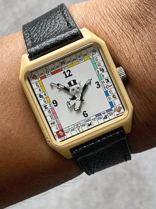 A vintage-style Monopoly wristwatch with a cream-colored case and black leather strap is worn on a wrist, featuring the classic Rich Uncle Pennybags mascot in a top hat surrounded by property cards around the dial.

The Monopoly theme ties into the "$CASHCAT" post, with the game board imagery symbolizing wealth, fortune, and financial success — reinforcing the optimistic "$CASHCAT to billions" sentiment.