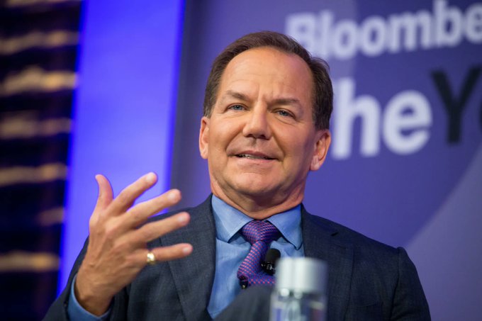 Paul Tudor Jones speaks at a Bloomberg event, gesturing while addressing an audience, with "Bloomberg" text visible behind him, in an image accompanying news about his firm Tudor Investment increasing its spot Bitcoin ETF holdings by 18.9% to over 688,529 IBIT shares worth approximately $22.9 million.