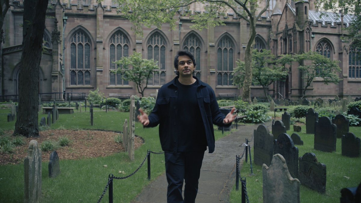 The image features a man walking down a path between two rows of headstones, with his arms outstretched as if he's about to make an important announcement or share some exciting news. The surrounding area includes trees and buildings, giving the scene a somewhat solemn atmosphere. The caption at the bottom of the image reads: "Very excited to see this go live! Welcome to @arbitrum".