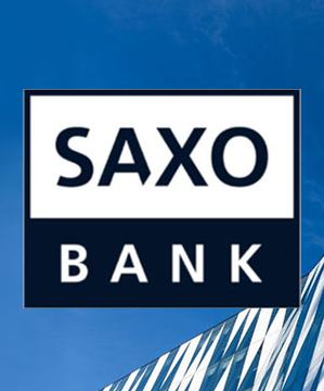 The Saxo Bank logo is displayed prominently against a blue sky and modern building backdrop, representing the institution that serves 1.5 million clients and has recently commented on Bitcoin's potential within the debasement trade.