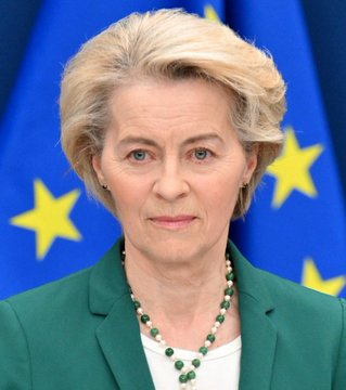 A woman with short blonde hair wearing a green blazer and beaded necklace stands in front of an EU flag featuring yellow stars. The image appears to depict a senior EU official, likely related to the warning about scammers impersonating EU regulators amid MiCA (Markets in Crypto-Assets) deadline issues.