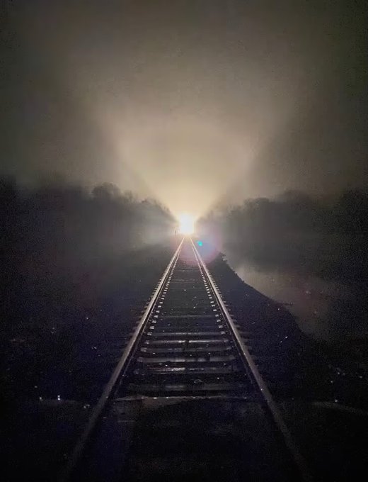 A solitary train approaches through foggy darkness at a railroad crossing in Jewett, Illinois, its headlight piercing the mist—a powerful symbol of the location where the photographer once attempted suicide in 2004 and where their Web3 journey's first mint, "Train for Death," was born on 8/19/2021.