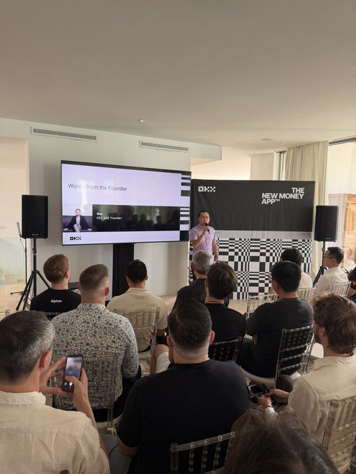 A speaker presents "The New Money App" at an OKX event, standing before a screen displaying "Word from the Founder" to an attentive audience, illustrating the company's role in building onchain financial infrastructure for emerging AI-driven economies.