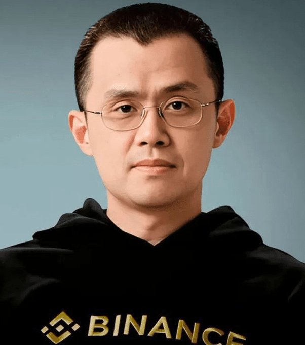 The image features a man wearing glasses and a hoodie with the word "BINANCE" printed on it. The man has short hair, and he appears to be looking directly at the camera. There are no other objects or texts present in the image.