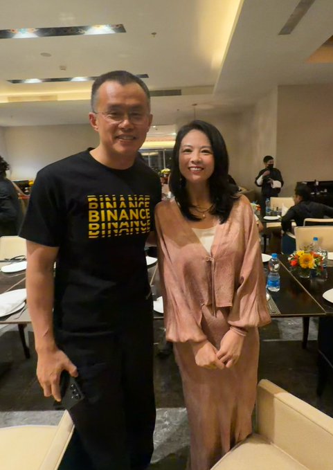 A man wearing a black "BINANCE" t-shirt poses with a woman in a pink outfit at what appears to be a Yzi Labs EASYResidency S4 event in Bhutan, matching the post about a gathering of long-term crypto and AI builders.