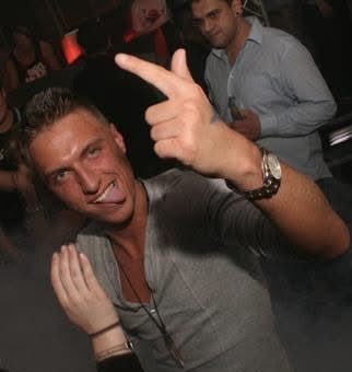 A young man in a dimly lit club setting playfully points at the camera while biting his lip, embodying the carefree party lifestyle of his past. The image starkly contrasts with the reflective caption, illustrating the "partying all the time" era before he found purpose through Bitcoin and personal growth.