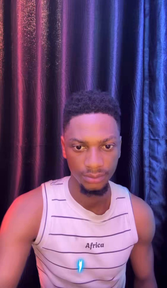 The image features a man wearing a white tank top with black stripes and a name tag that reads "Africa" who appears to be posing for a photo. The background of the image consists of purple curtains, which adds an interesting visual element to the scene. The caption below the image provides information about a trading platform called WEEX, offering zero-fee trading benefits for users.