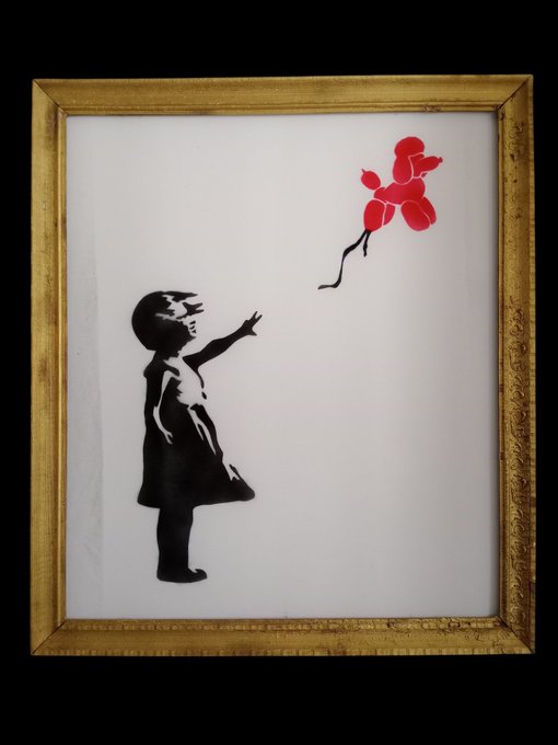 A framed Banksy-style stencil artwork featuring a small black silhouette of a girl reaching toward a red balloon floating away.