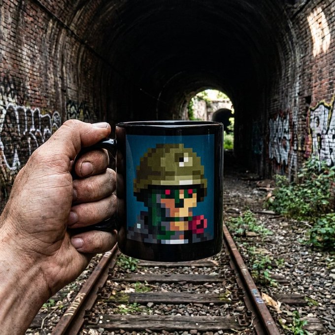 A hand holds a black mug featuring pixel art of a soldier with a helmet and glowing red eyes, set against the backdrop of an abandoned, graffiti-covered brick tunnel with railroad tracks.