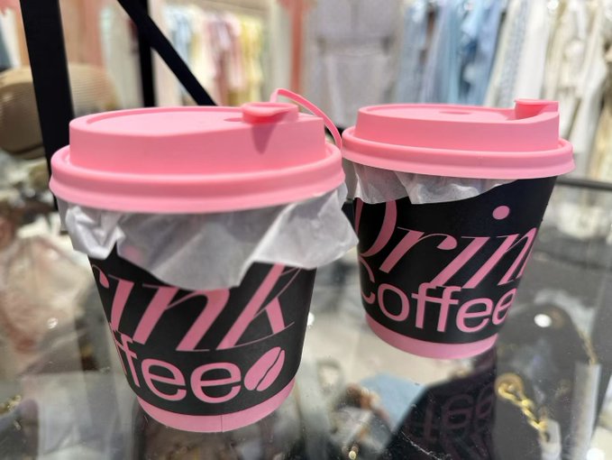 Two pink and black paper coffee cups from "pink coffee" sit on a glass surface with tissues sticking out from under the lids.