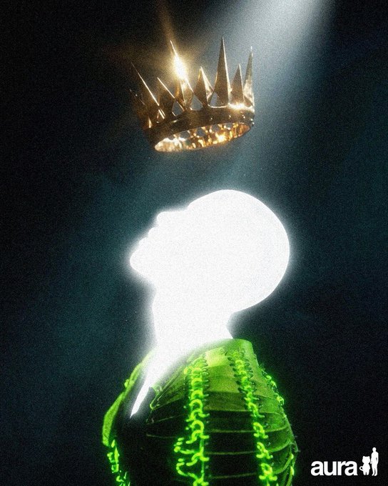 An artistic, grainy image of a silhouetted figure in a green top with a glowing white head, looking up at a floating golden crown illuminated by a light beam, with the "aura" logo in the corner.