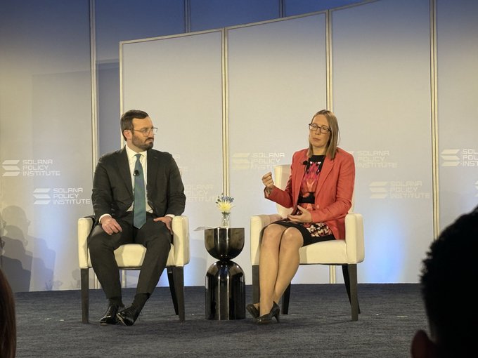 A panel discussion at the Solana Policy Institute featuring a man in a dark suit and a woman in a red blazer seated on white chairs on a stage.