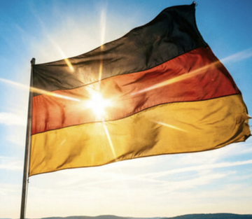 The German flag waving against a bright sky with the sun shining through it.
