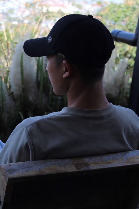 The image shows a man wearing a black baseball cap sitting down with his back facing the camera, looking out at something outside of the frame. The caption reads "BTC Tăng rồiETH cũng tăng rồi SOL cũng đang chuẩn bị tăng !!! Mà anh em rời thấy ai nói đến Crypto vẫn còn tiền mà , ở lại đi , lấy tiền về đi anh em". The man's hat and the caption are both black in color.