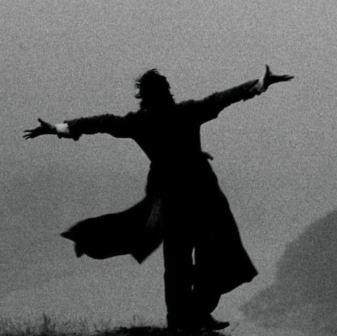 A black-and-white silhouette photograph of a person standing with arms outstretched in a dramatic pose against a hazy background.