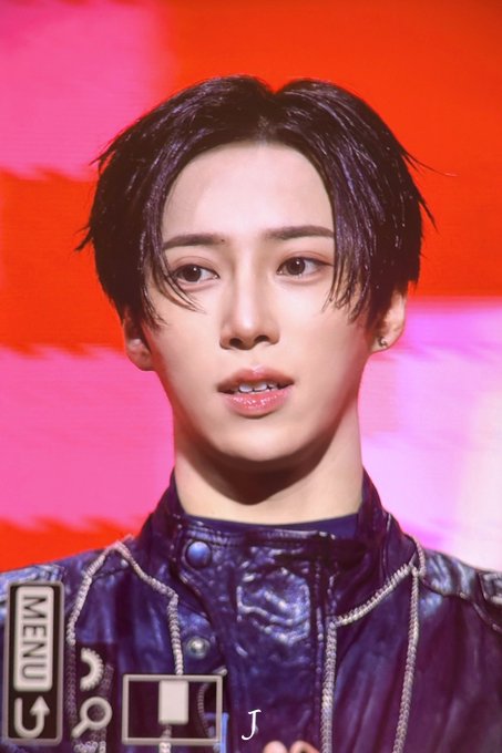 A close-up portrait of a young man with dark hair wearing a dark jacket, set against a vibrant pink and red background, with a partial "MENU" graphic overlay on the left.