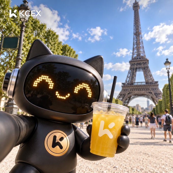 A promotional image for KCEX featuring a black robot/cat-like character holding an orange drink with the Eiffel Tower in the background.