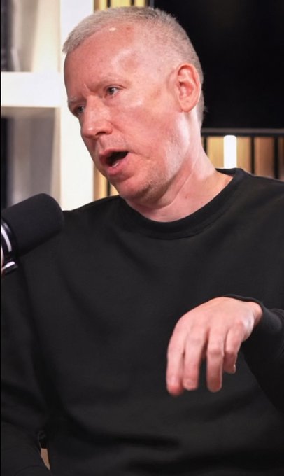 Portrait photo of a fair-haired man in a black shirt speaking into a microphone.