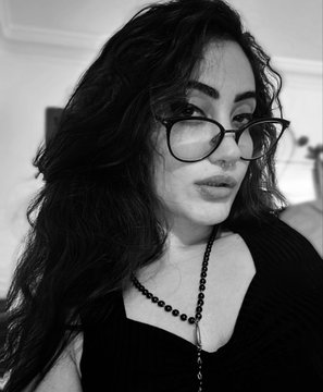 A black and white portrait shows a woman with dark wavy hair wearing glasses and a black top, gazing off-camera.