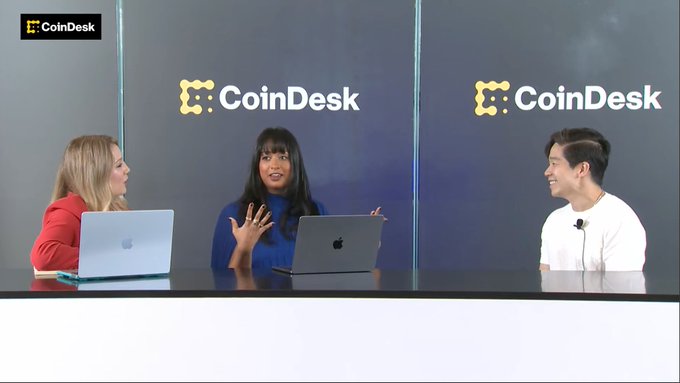 The image shows a CoinDesk TV broadcast featuring three people seated at a desk with laptops, with Eddie Zhang (right) being interviewed alongside two female hosts, all set against a backdrop prominently displaying the CoinDesk logo, matching the post's announcement of his live appearance on CoinDesk TV.
