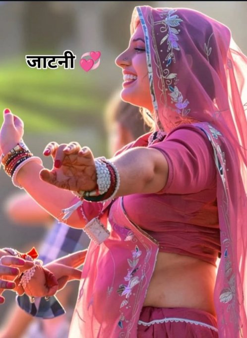 A smiling woman in traditional pink Rajasthani attire with elaborate henna designs on her hands, wearing jewelry and bangles, with Hindi text 'जाटनी' and pink heart emojis overlaid.
