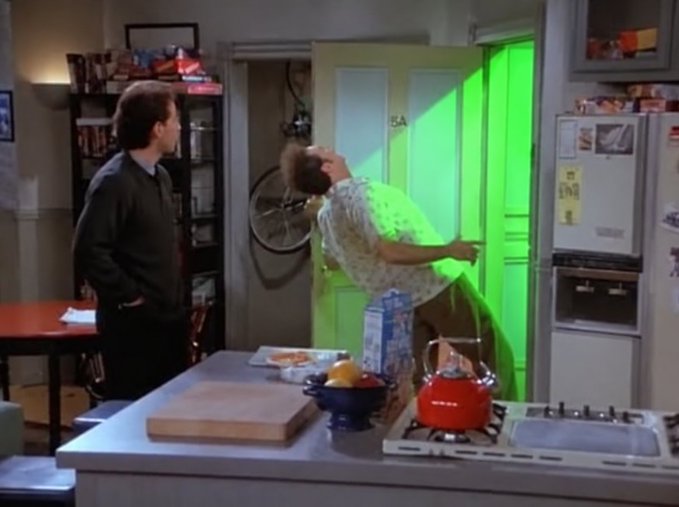 A scene from the TV show Seinfeld showing George Costanza dramatically flung backward with green smoke/sparks shooting from his chest, while Jerry Seinfeld watches in their kitchen.