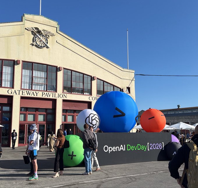 An outdoor scene at the OpenAI DevDay (2026) event showing large colorful orbs including a blue one with the GPT logo, in front of the historic Gateway Pavilion building.
