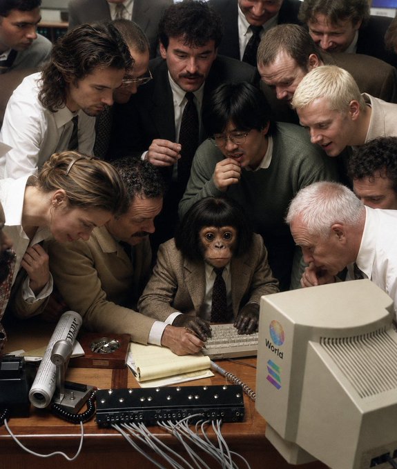 A chimpanzee in a business suit sits at a computer with a "Wonta" monitor, surrounded by a crowd of onlookers intently watching as it types on a keyboard. The image humorously connects to the post's message about creativity and being "locked in" on-chain, using the metaphor of a focused monkey artists to represent dedication and inspiration from the mentioned mentors.
