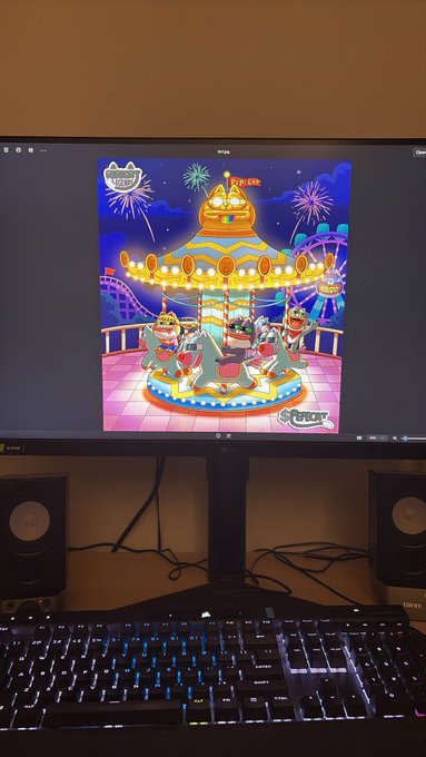 A computer monitor displays a colorful illustration of three characters riding a carousel, with a backlit keyboard visible in the foreground.