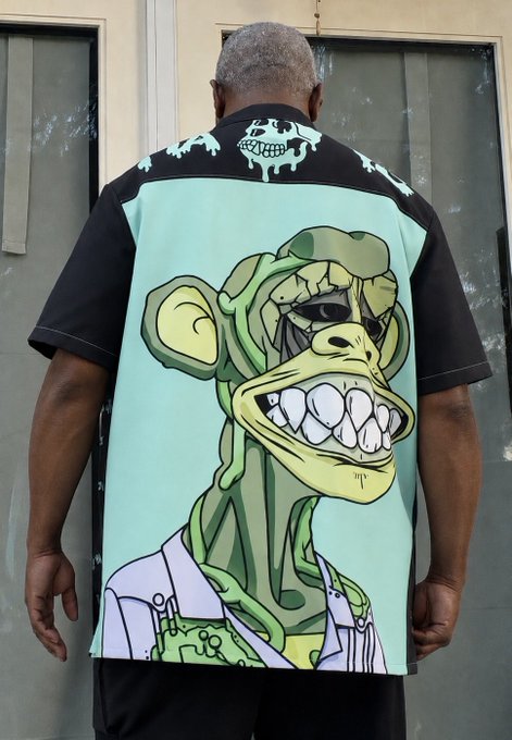 A man viewed from behind wearing a teal and black short-sleeve shirt featuring a large cartoon graphic of a grinning ape or gorilla character.