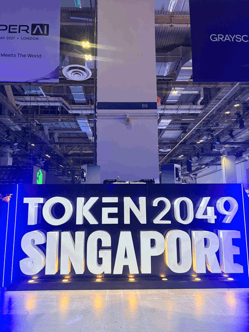 An illuminated blue event sign reading 'TOKEN 2049 SINGAPORE' displayed inside a large convention hall.