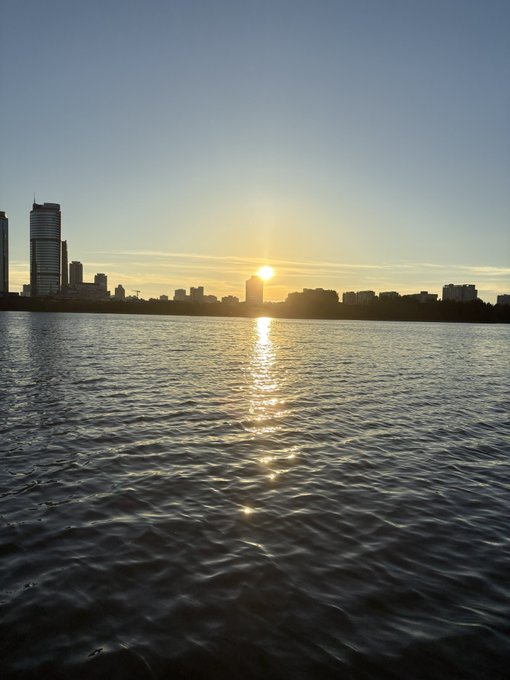 A sunset over a calm city skyline reflects golden light across rippling water. The serene image contrasts with the post's lament about selling Marscoin too early, symbolizing a parting moment as the author says goodbye to the missed opportunity and looks toward the next investment.