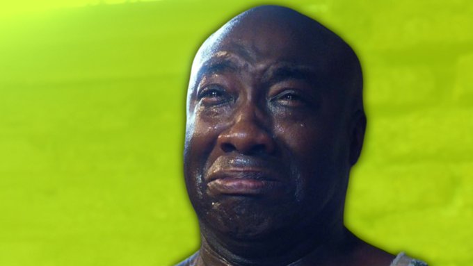 A close-up of a bald, sweating Black man crying against a yellow background.
