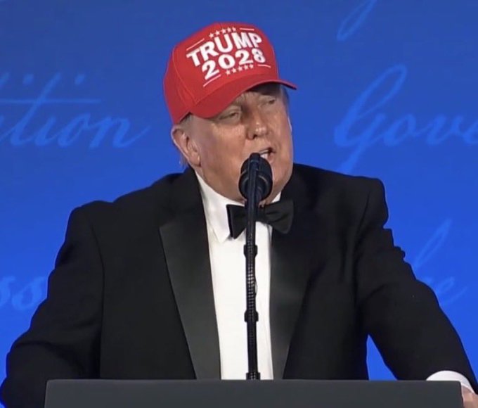 A man in a black tuxedo and red "TRUMP 2028" cap speaks at a podium with a microphone against a blue backdrop, prompting reflection on satisfaction with cryptocurrency policy under Donald Trump's potential second term. The image ties to the post by visually representing the Trump administration's continued influence and its implications for crypto regulation.