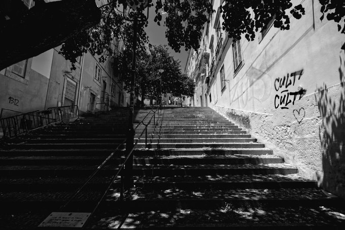 A black and white photograph of stone steps leading up a narrow street, with graffiti reading "CULT CULT" and a heart drawn on the wall to the right.