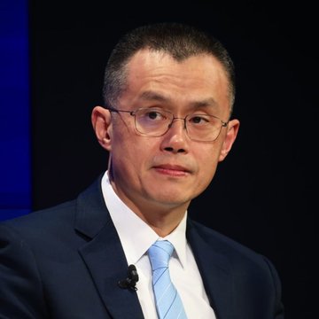The image features an older man wearing glasses, a suit, and a blue tie. He appears to be speaking or giving a presentation at a conference. The caption reads "CZ says a crypto super cycle might be late...". This statement is likely related to the man's speech or topic of discussion during his presentation.