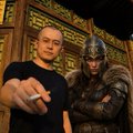 A bald man with a cigarette stands in front of a samurai statue near a gold-trimmed shrine, evoking a warrior's determination that mirrors the post's message of momentum and battles being won in trenches and battlegrounds for TCryptochicks (TCC) on BNB.