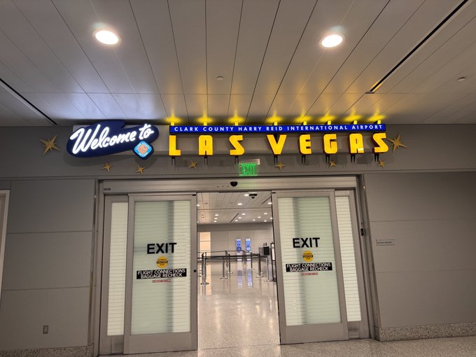 An illuminated 'Welcome to LAS VEGAS' sign above automatic exit doors at Clark County Harry Reid International Airport.