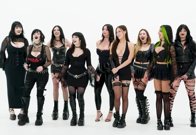 A group of nine goth-styled women poses together in a studio setting, wearing an assortment of black outfits including corsets, fishnet stockings, platform boots, and one shirt reading "WINNIE A COOP." The image's coordinated edgy aesthetic mirrors the post's tongue-in-cheek "stock market" framing of the goth "fad," illustrating the very aesthetic being humorously declared as having peaked.