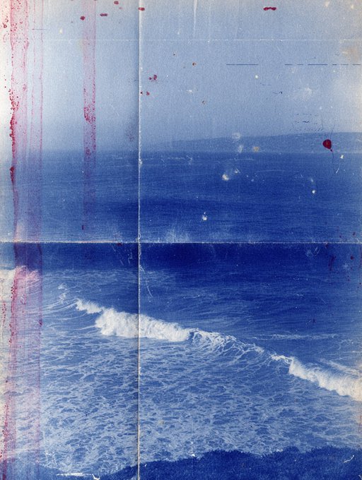 An artistic print of ocean waves with white surf against deep blue water, featuring visible red and white speckles and drips on the surface.
