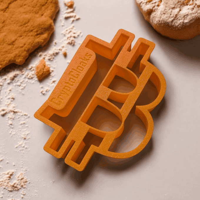 An orange 3D-printed cookie cutter shaped like a dollar sign with "HD BAKS" text on it, displayed on a white surface next to cookies and scattered flour.